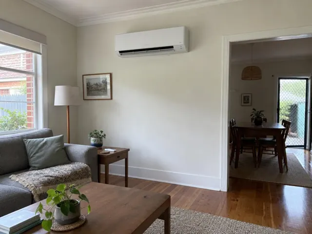Wall-mounted split system above a living room sofa in a light painted home interior in Mile End